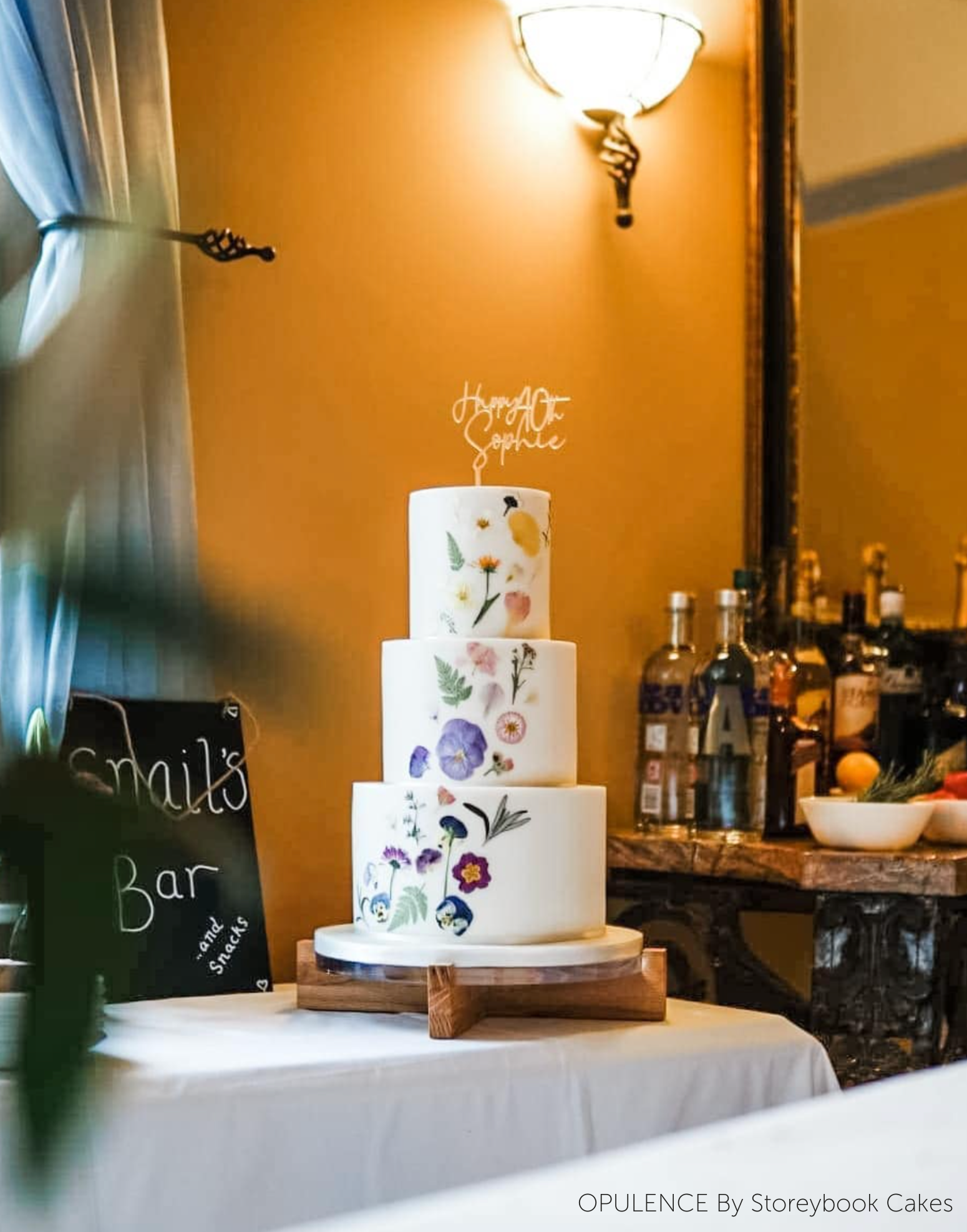 A white three layer cake with floral decorations stood on a Handcrafted Solid Oak Cake Stand - Prop Options