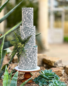 A white cake with detailed dark green floral patterns stood on The Teardrop Scandinavian Birch Cake Stand - Prop Options